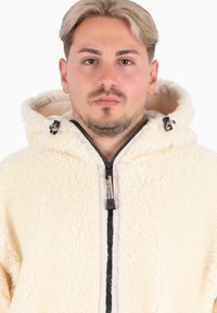 Crème-kleurige fleece zip-up hoodie met een gestructureerde buitenkant, zwarte rits en een trekkoord-capuchon. Heeft een zachte binnenvoering.