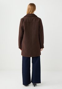 Brauner Wollmantel mit einem Kragen, langen Ärmeln und geradem Schnitt. Kombiniert mit weit geschnittenen dunklen Jeans. Minimalistisches Design, keine sichtbaren Muster.