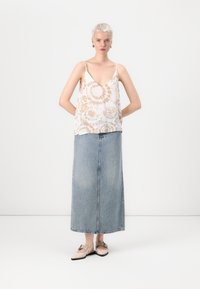 Kevyt, beige ilman hihoja oleva toppi, jossa on spiraalinen sitruunaväri, yhdistettynä pitkään siniseen farkkuhameeseen ja beigenvärisiin ballerinatossuihin, joissa on nauhatammi.