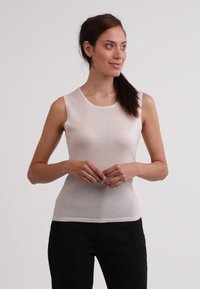 Leichtes, ärmelloses Cremetop mit rundem Ausschnitt und taillierter Silhouette. Glattes Material mit minimalen Nähten, kombiniert mit schwarzen Hosen.