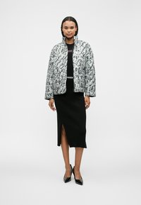 Διακοσμημένο μπουφάν σε μαύρο και άσπρο αφηρημένο σχέδιο, συνδυασμένο με μαύρο ριμπ μεσάτο φόρεμα με άνοιγμα στο πλάι και μαύρες μυτερές γόβες.