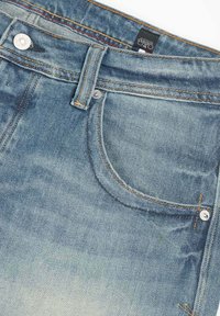Jeans de mezclilla azul claro con un aspecto desgastado, que cuentan con un diseño clásico de cinco bolsillos, herrajes de metal y costuras en contraste.
