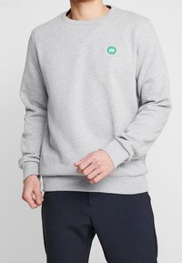 Felpa grigia in misto cotone, con scollatura a girocollo e polsini a costina. Logo circolare verde sul lato sinistro del petto.