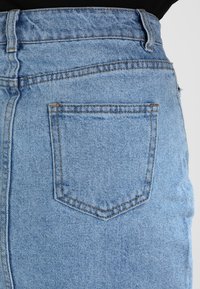 Světle modrá džínsová sukně s vysokým pasem, s jednou zadní kapsou a viditelnými švy. Hladká textura, klasický design.