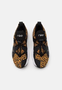 Zapatillas deportivas negras y naranjas con un diseño de estampado de leopardo, textura suave y cordones elásticos. Logo de Nike en la lengüeta negra. Punta redonda.