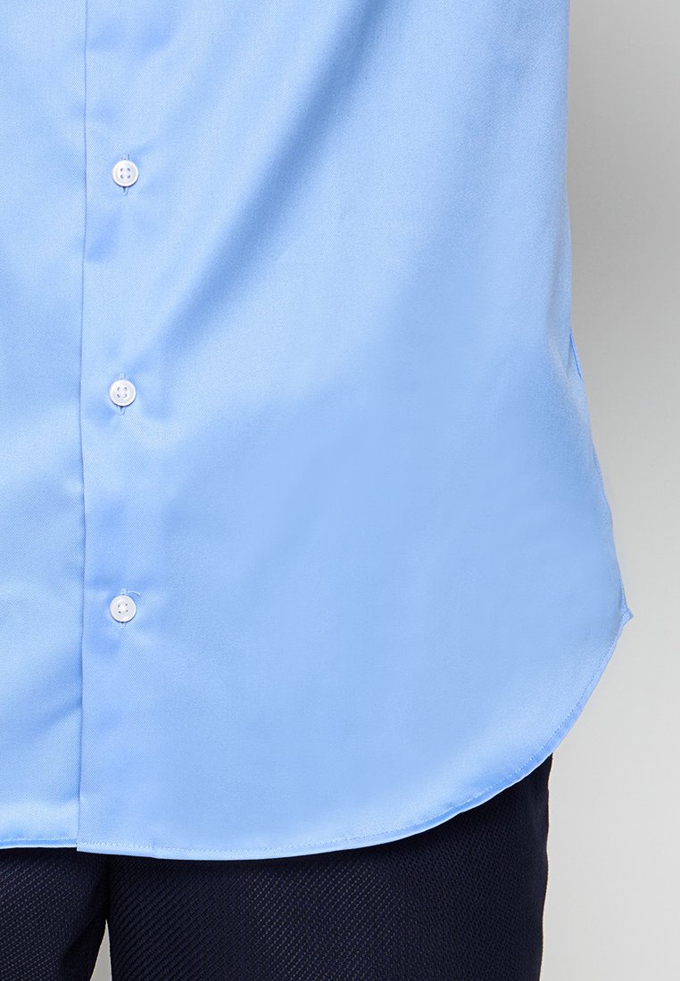Himmelblaues Hemd mit Knopfleiste, glatter Textur, abgerundetem Saum und weißen Knöpfen, teilweise in dunkle Hosen gesteckt.