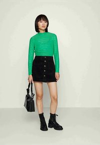 Πράσινη ριγέ μακρυμάνικη μπλούζα, μαύρη φούστα με κουμπιά μπροστά, μαύρες μπότες στρατού και μια υφασμάτινη μαύρη τσάντα.