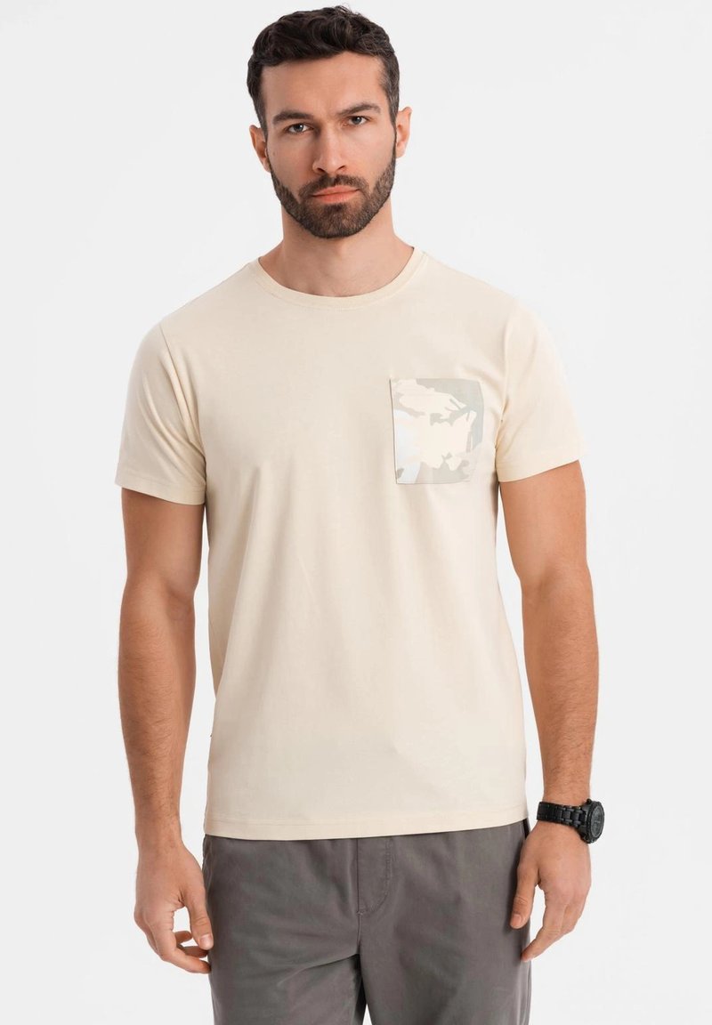 Camiseta de algodón beige con cuello redondo y mangas cortas. El bolsillo en el lado izquierdo del pecho presenta un ligero patrón de camuflaje. Diseño simple y casual.