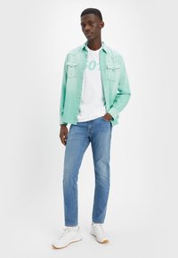 Majolkasto zelena denim srajca, bela grafična majica, svetlo modri kavbojke in bele teniske. Priložnostna obleka z gumbnimi žepi na srajci.