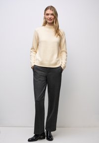 Pull en col roulé crème avec ourlet côtelé, associé à un pantalon large gris charbonneux, complété par des bottines noires. Tissu à texture lisse.