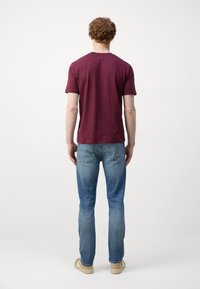 Burgundi pamut póló rövid ujjakkal, világoskék farmernadrággal párosítva. Testhez álló fazon, egyenes szára, minimalista hátsó zsebbetétekkel.