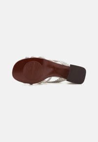 Sandal in tessuto aperto con suola in gomma marrone, dotata di una soletta testurizzata e un tacco basso a blocco. Il colore è beige chiaro con accenti scuri.