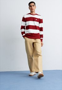 Jersey de rayas rojas y blancas con cuello redondo, pantalones beiges y zapatillas blancas con suelas de color marrón claro. Diseño sencillo y ajuste casual.
