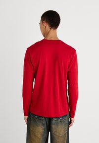 Rød langærmet T-shirt lavet af blødt bomuld, med rund halsudskæring og en afslappet pasform. Bæres sammen med slidte blå jeans.