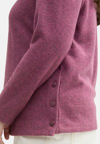 Pull en tricot magenta avec une finition texturée, manches longues et cinq boutons violets le long de la couture latérale.