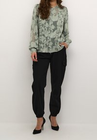 Light green layered blouse with floral pattern and ruffle details, paired with black cargo pants. Black stiletto heels complete the outfit.