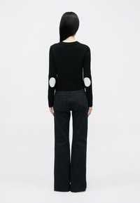 Suéter negro de punto con dobladillo acanalado, que presenta coderas redondas blancas, combinado con pantalones negros acampanados. Tela de textura suave.