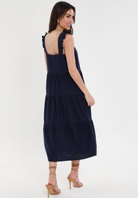 Abito midi a strati di un blu navy con spalline arricciate e schiena scoperta, realizzato in tessuto leggero; presenta una vestibilità fluida e rilassata.