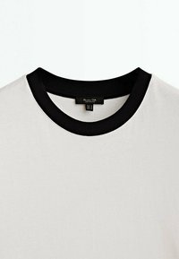 T-shirt blanc à col rond avec un col côtelé noir contrastant et une étiquette de marque noire visible à l'intérieur de l'encolure.