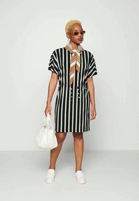 Vestido listrado em preto e branco com mangas curtas, frente com botões e detalhe de laço; combinado com ténis brancos e uma bolsa branca.