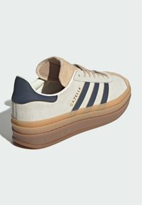 Adidas Gazelle sneaker in cream suede and navy accents. Features three navy stripes, beige suede heel, and a gum rubber sole.