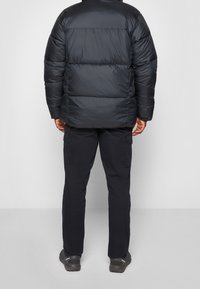 Černá péřová bunda s horizontálním prošitím, vybavená vysokým límcem a doplněná o tmavé cargo kalhoty a hnědé outdoorové boty.