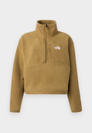 Bež flis pulover s poluverzom ovratnikom na patentni zatvarač, prednjim džepom i elastičnim rubom; ima mekanu, teksturiranu površinu i bijeli logotip.