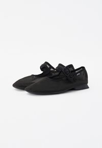 Ballerine in rete nera con punta affusolata, tacco basso e cinturino regolabile con fibbia. Il materiale è texturizzato con un design traspirante.