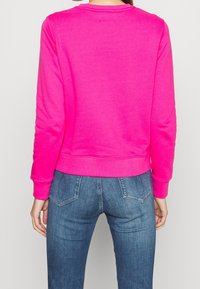 Fuchsia sweatvest met lange mouwen, ronde hals en geribde manchetten, gecombineerd met blauwe spijkerbroek met vijfzakkenontwerp.