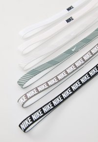 Set tankih elastičnih gumica za kosu u bijeloj, svijetlo sivoj, zelenoj s prugama, tamno sivoj i crnoj boji, s ponovljenim "NIKE" brendom.