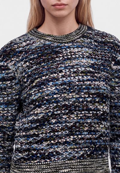 Gros plan d'une personne portant un pull en tricot texturé multicolore avec un col rond et des bords-côtes à l'ourlet et aux poignets.