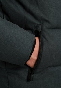 Doudoune gris foncé avec une poche zippée à l'avant, texture du tissu légèrement brillante et poignets élastiques pour un ajustement confortable.