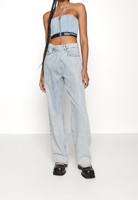 Mujer vistiendo un top cortito de mezclilla azul claro y unos pantalones vaqueros de pierna ancha y cintura alta a juego, con zapatos de plataforma negros.