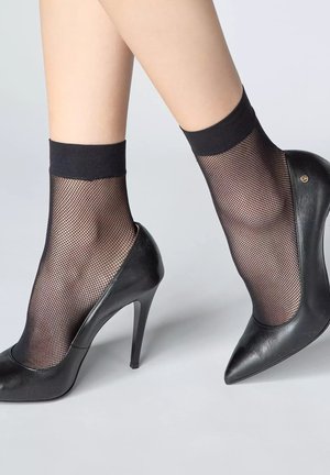 Czarne szpilki z ostrym noskiem, wykonane z gładkiej skóry, połączone z czarnymi skarpetkami z siateczki do kostek, ozdobionymi solidnym paskiem na górze.