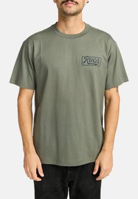Olivegrünes Baumwoll-T-Shirt mit lässiger Passform, kurzen Ärmeln und einem Frontgrafik-Logo in einer kontrastierenden dunklen Farbe.