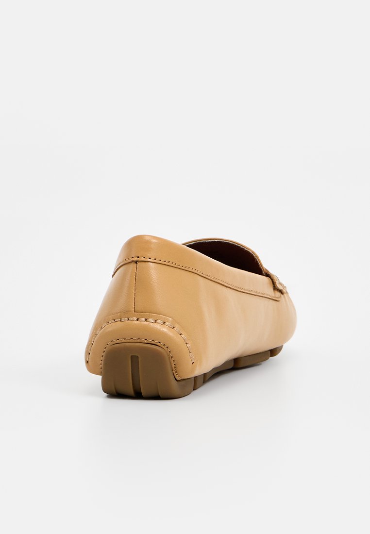 Mocassin en cuir tan avec couture visible et semelle en caoutchouc segmentée, présenté de dos et légèrement de côté sur fond blanc.