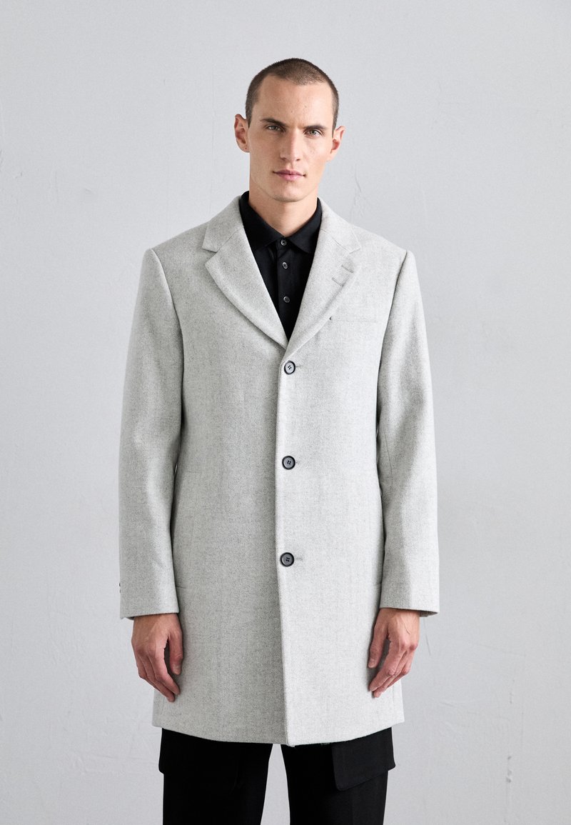Light gray wool coat with a tailored fit, notched lapels, three buttons, and a smooth texture. Worn over a black shirt.