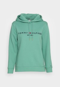 Sudadera verde claro de Tommy Hilfiger con cordones frontales, texto del logo y emblema de la bandera en el pecho, y pequeño emblema de la bandera en el puño de la manga izquierda.