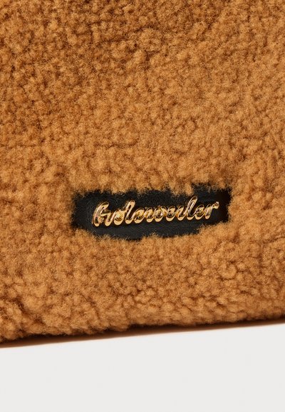 Tecido castanho com textura e aparência felpuda, apresentando um logótipo em dourado "Gelenwiller" numa etiqueta de couro preto.