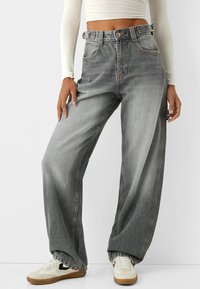 Jasnoszare, wysokie dżinsy z denimu o szerokich nogawkach, z pomarańczowymi przeszyciami i pętlą na pasek. Stylizowane z białymi trampkami.