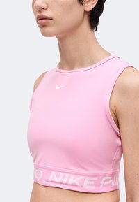 Gros plan d'une personne portant un haut de sport rose sans manches Nike avec un logo blanc sur la poitrine et une bande de marque à la taille.