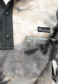 Κοντινό πλάνο μπεζ, γκρι και μαύρου fleece μπουφάν Columbia Sportswear με θήκη στο στήθος με φερμουάρ και πατιλέτα με κουμπιά πατιλέτας.