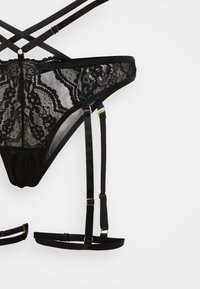 Sort blondetrusse med gennemsigtige paneler, elastiske stropper og guldfarvede hardware-detaljer. Designet med en stropdetaljeret, kompleks ryg.