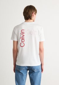 Hvitt bomull T-skjorte med stor rød "Calvin Klein" tekstdesign på baksiden. Korte ermer, rund hals og avslappet passform.