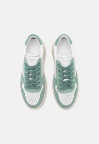 Paire de baskets basses blanches et vertes avec des orteils perforés et des lacets verts, vue depuis le dessus sur un fond blanc.