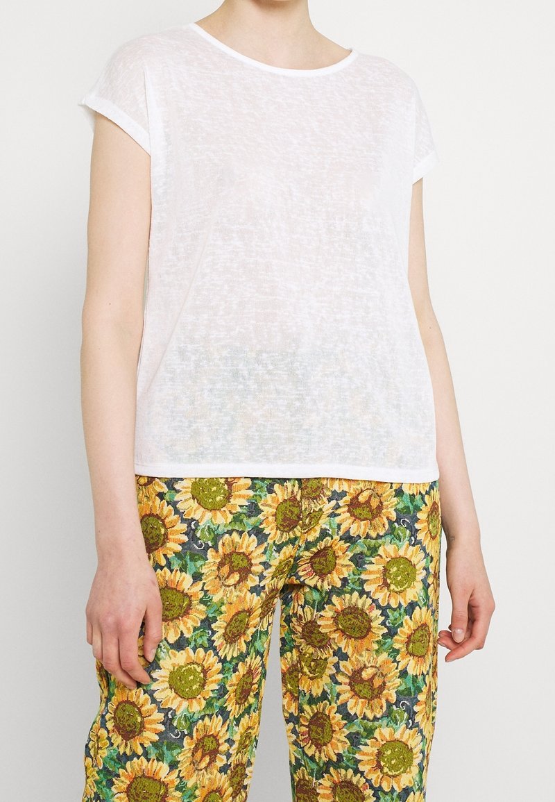 Top corto de manga corta blanca con un tejido texturizado y transparente, combinado con pantalones verdes que presentan un estampado de girasoles en amarillo y marrón.