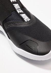 Černá sportovní bota s texturovaným svrškem, štíhlým designem, elastickým páskem a bílým logem Nike na gumové podrážce.