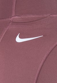 Zbliżenie na bordową tkaninę sportową z dokładnym przeszyciem oraz białym logo Nike w kształcie łuku.