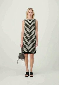 A kötött ujjatlan ruha fekete-fehér cikk-cakk mintával, kerek nyakkivágással és egyenes szabással rendelkezik. Fekete, csúsztatós szandállal és táskával viseli.