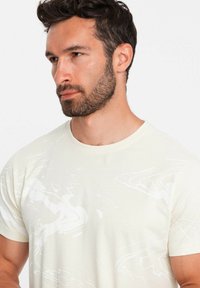 Light beige t-shirt made of soft fabric featuring a subtle abstract white pattern, short sleeves, and a crew neck design.